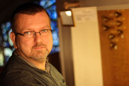 Michael Georgi sitzt an der Orgel, das Licht ist angeschaltet, er trägt eine Brille und er schaut in die Kamera. - Copyright: Thomas Moll 